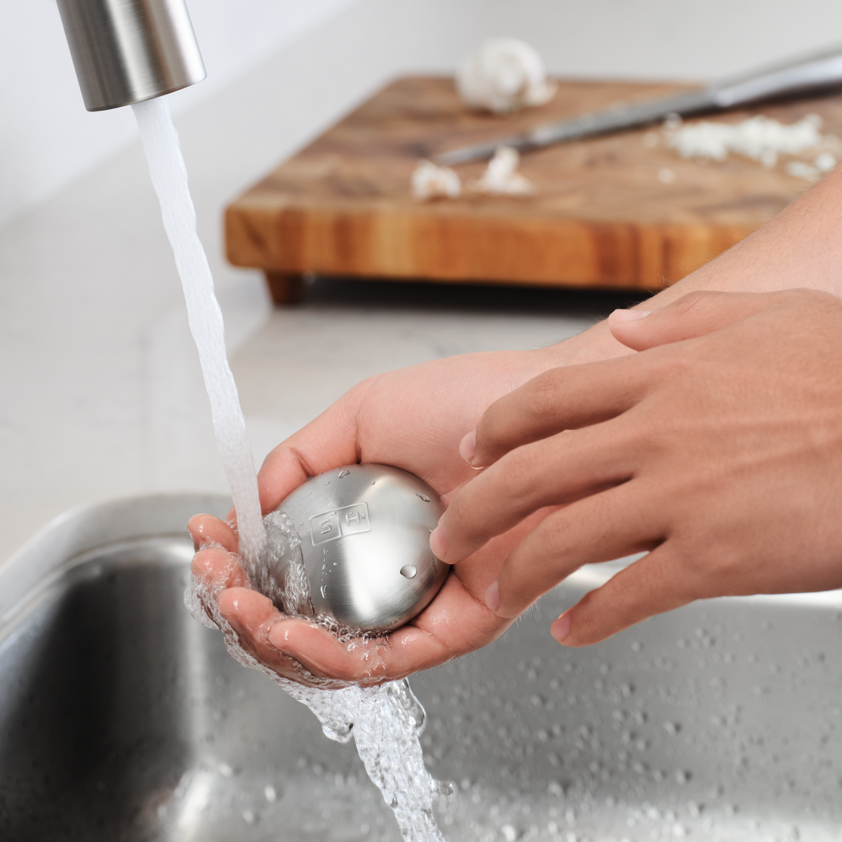 Lifestyle view of Simplehuman Brushed Stainless Steel Soap Bar used under running water, removing kitchen odors.