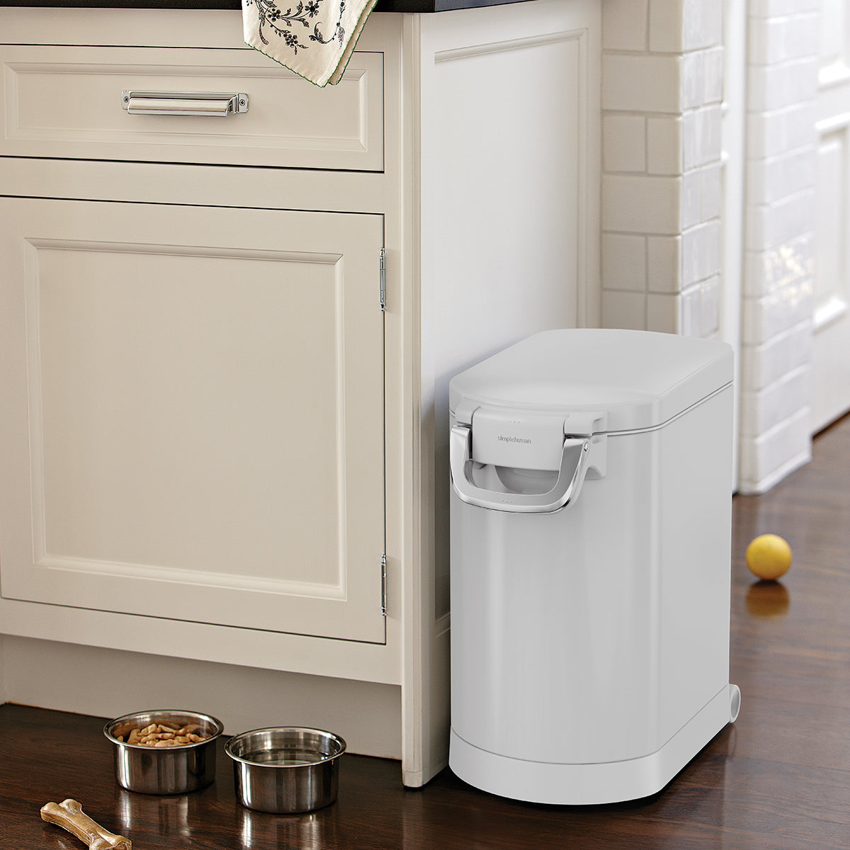 Corner view of Simplehuman Medium Pet Food Can, White, stored in kitchen nook with food bowls, secure airtight seal.