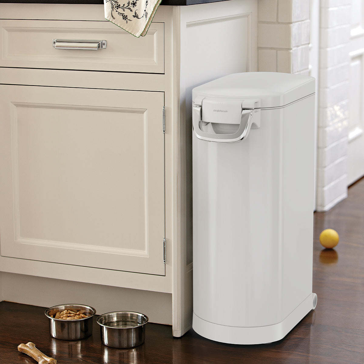 Kitchen view of Simplehuman White X-Large Pet Food Can next to pet bowls. Airtight locking handle and mobility wheels.