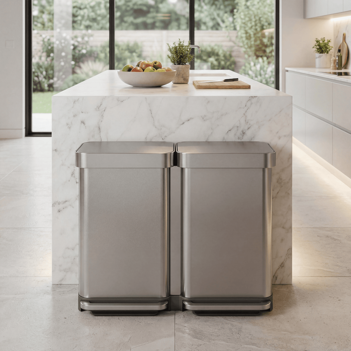 Simplehuman's 90L Step Recycler in Brushed in a modern contemporary kitchen with white counters and a marble island in the center of the kitchen with fruits, plants, and a cutting board on top. The image focuses on the can in the center.