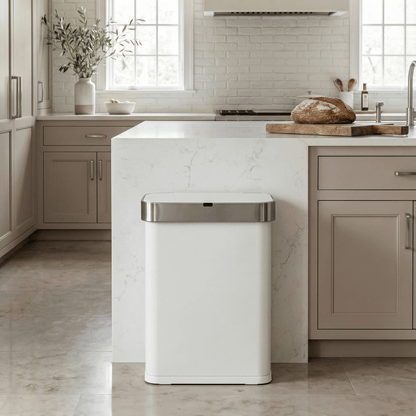Simplehuman's 58L Sensor Can in White in a modern kitchen setting with neutral cabinetry, white marble counter tops and walls, with slight greenery and natural light in the background.